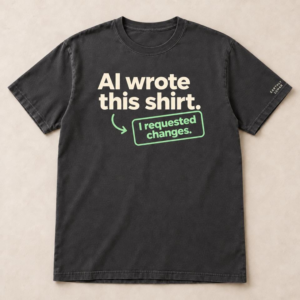 Charcoal tee with 'AI wrote this shirt.' in big cream letters and a mint arrow pointing to a tag reading 'I requested changes.'