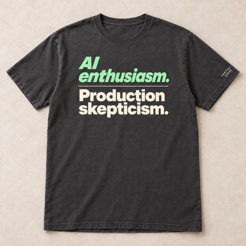 Charcoal tee with 'AI enthusiasm.' in slanted mint letters over 'Production skepticism.' in bold cream letters