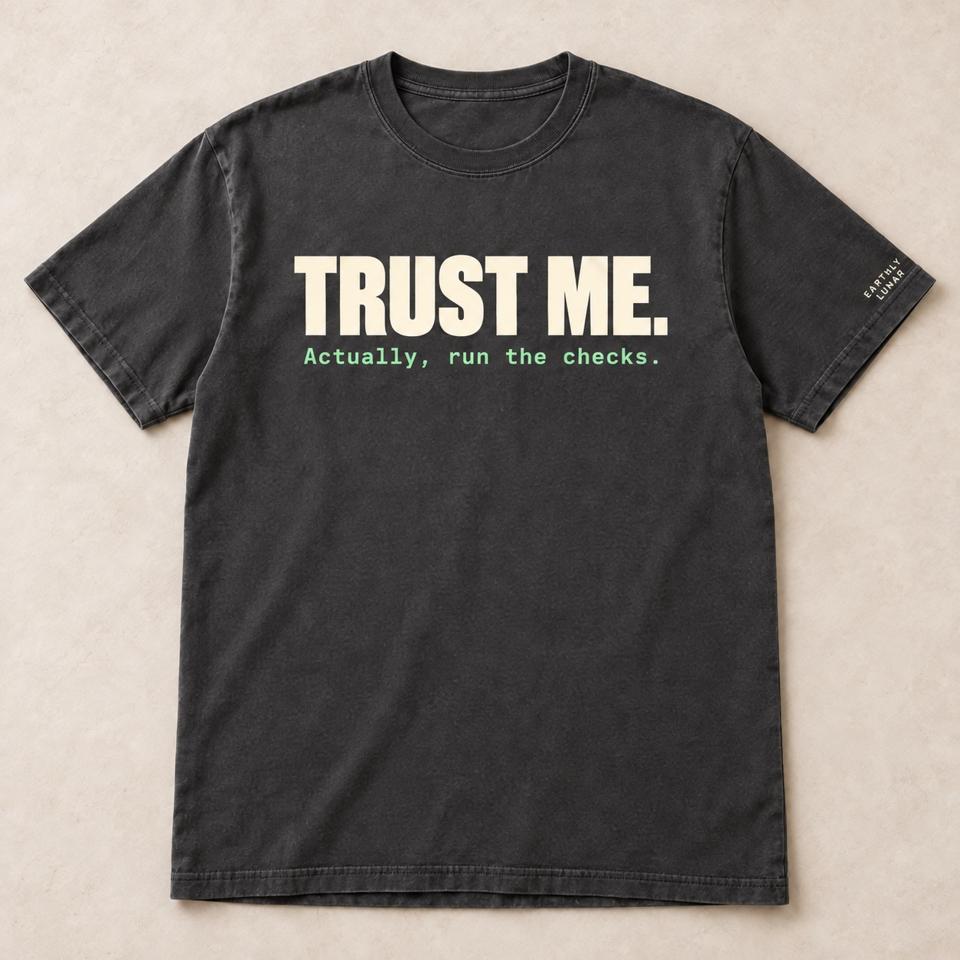 Charcoal tee with 'TRUST ME.' in big cream capitals over 'Actually, run the checks.' in small mint typewriter type