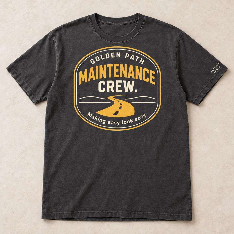 Charcoal tee with an amber badge reading 'GOLDEN PATH MAINTENANCE CREW.' around a winding road, and 'Making easy look easy.'