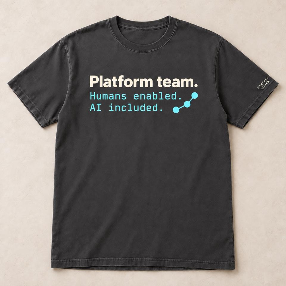 Charcoal tee with 'Platform team.' in cream over 'Humans enabled. AI included.' in cyan typewriter type beside a small node graph