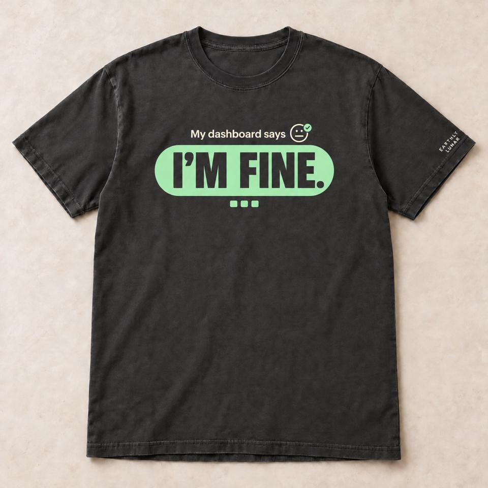 Charcoal tee with 'I'M FINE.' in oversized charcoal capitals inside a mint pill, beneath small cream 'My dashboard says' and a neutral face with a mint check