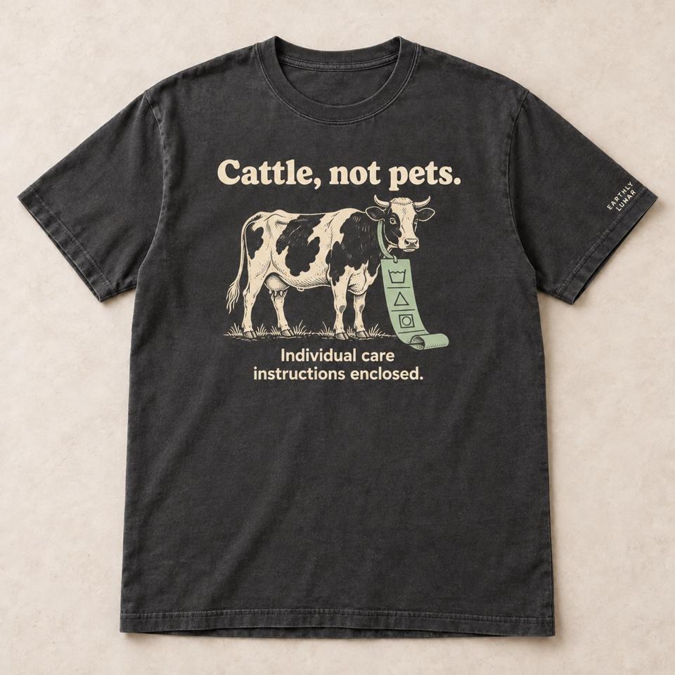 Charcoal tee with cream 'Cattle, not pets.' above an illustrated cow wearing a long mint care label, over 'Individual care instructions enclosed.'